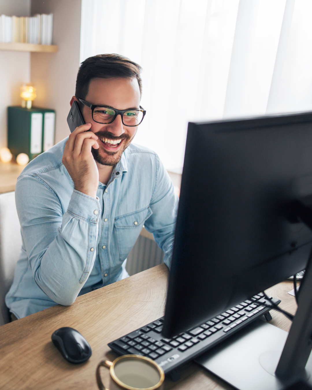 A man on the phone working at a home office desk with dual monitors